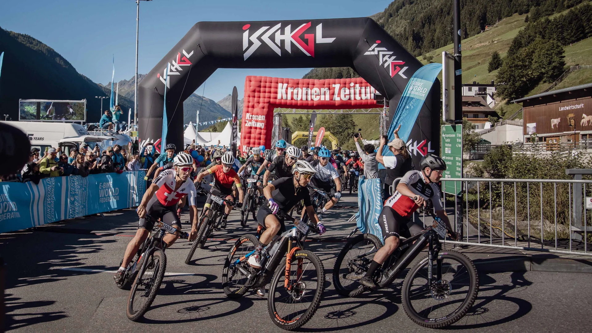 Wir sind E-Bike. Mountainbike-Rennen mit Fahrern unter einem Ischgl-Bogen in den Alpen