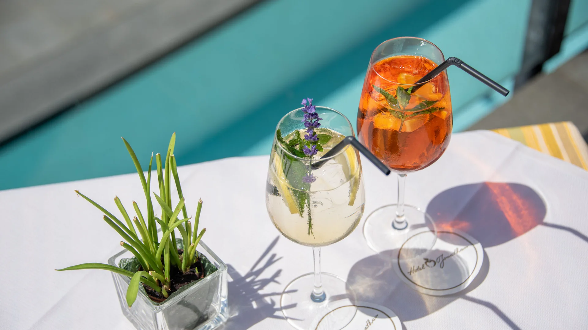 Zwei bunte Cocktails mit Kräutern auf weißer Tischdecke am Pool