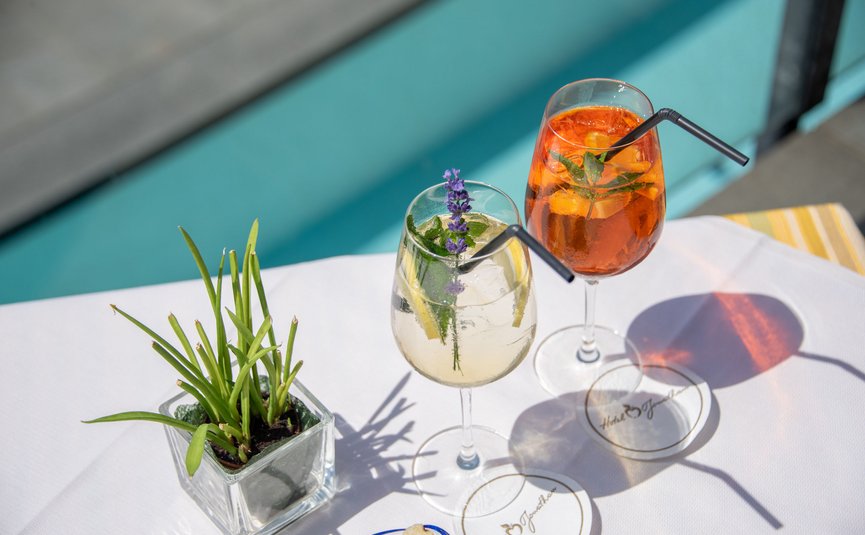 Zwei bunte Cocktails mit Kräutern auf weißer Tischdecke am Pool