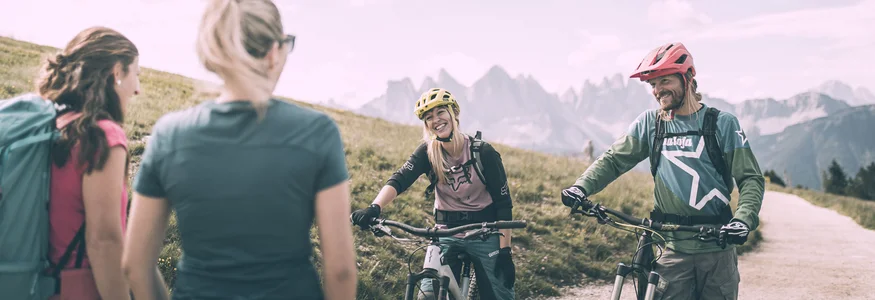 Biken á la Brixen © Brixen Tourismus - Manuel Kottersteger Zwei Mountainbiker mit Helm und zwei Wanderer im Gebirge bei sonnigem Wetter