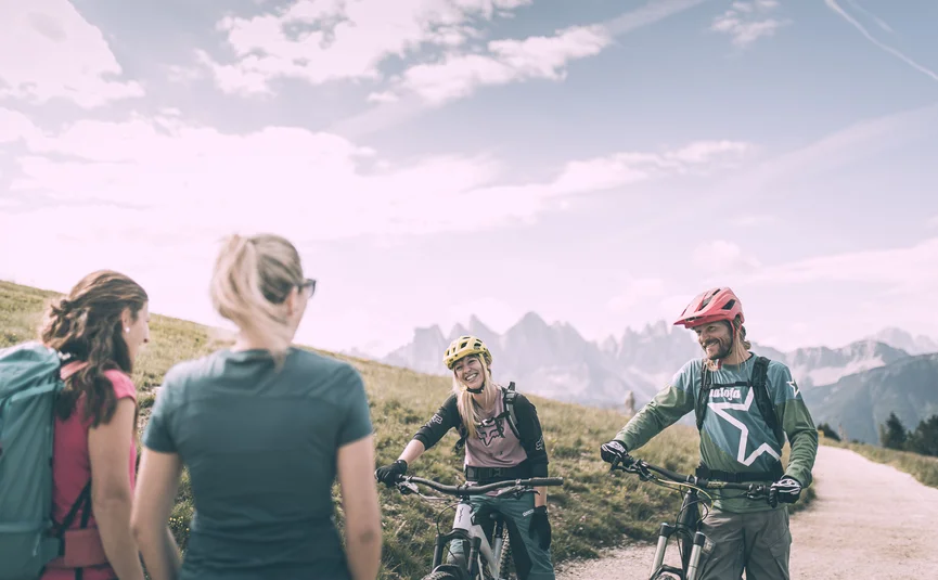 Zwei Mountainbiker mit Helm und zwei Wanderer im Gebirge bei sonnigem Wetter