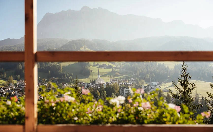 Blick durch ein Fenster auf Dorf, Blumen und Berge im Hintergrund