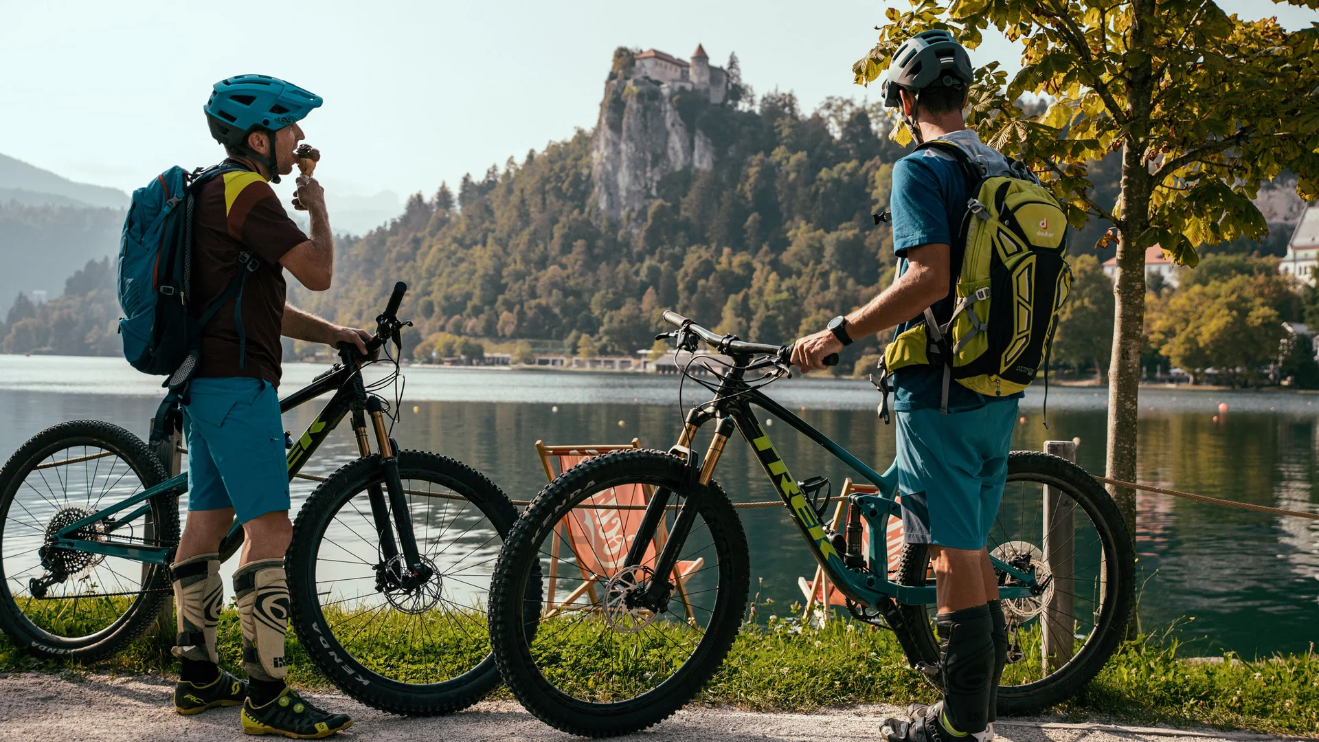 Dein Julische Alpen-Guide © Felix Saller Zwei Radfahrer machen Pause an einem See mit Berg und Schloss im Hintergrund