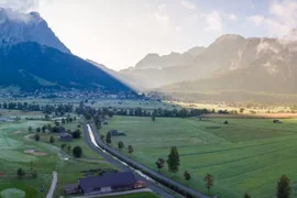 3=4 Tage Zugspitze Spätsommer inkl. 3 Tage Z-Ticket Panoramisch uitzicht op een groene vallei met wegen en met wolken bedekte bergen