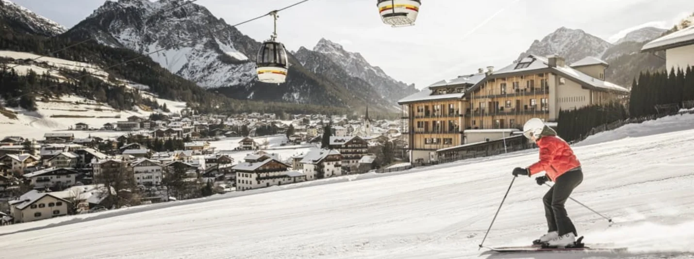 Skifahrer mit roter Jacke neben Seilbahn in verschneitem Bergdorf