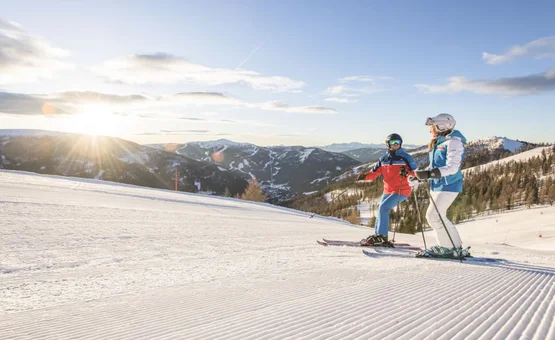 Twee skiërs op vers geprepareerde piste bij zonsondergang in de bergen