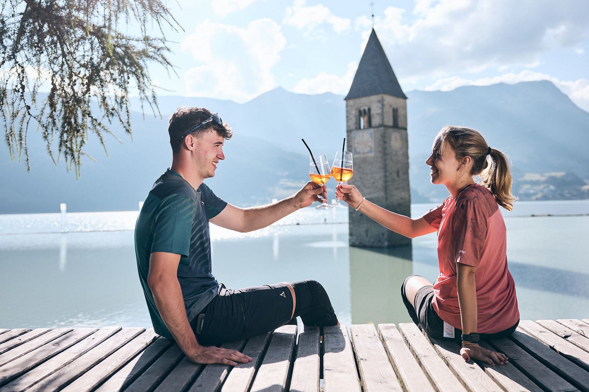Junges Paar stößt mit Aperol am gefluteten Kirchturm in Reschen an.