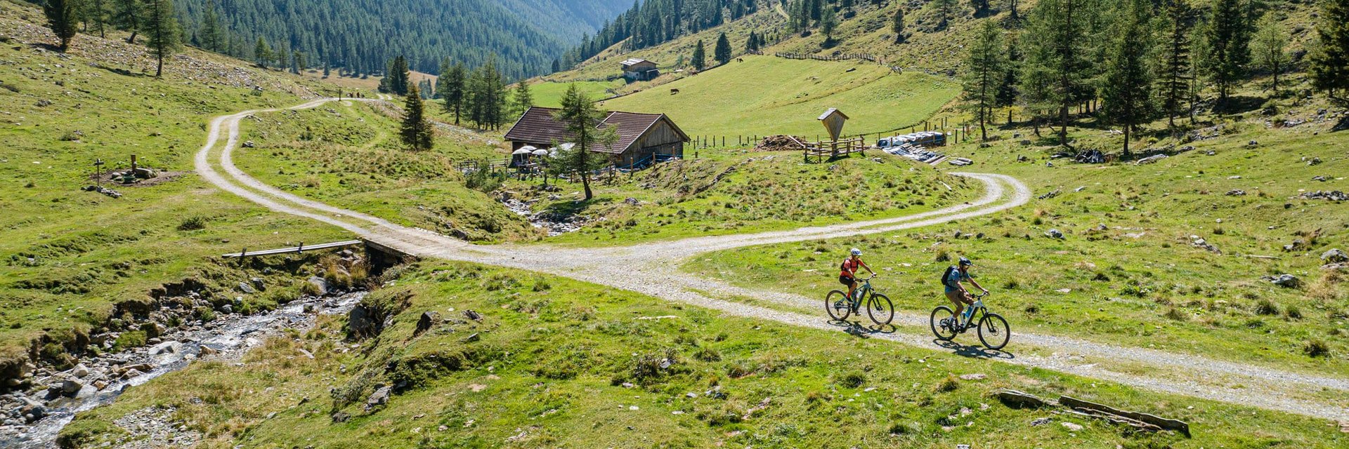 Two cyclists riding on a mountain trail through green alpine scenery