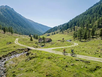 Two cyclists riding on a mountain trail through green alpine scenery