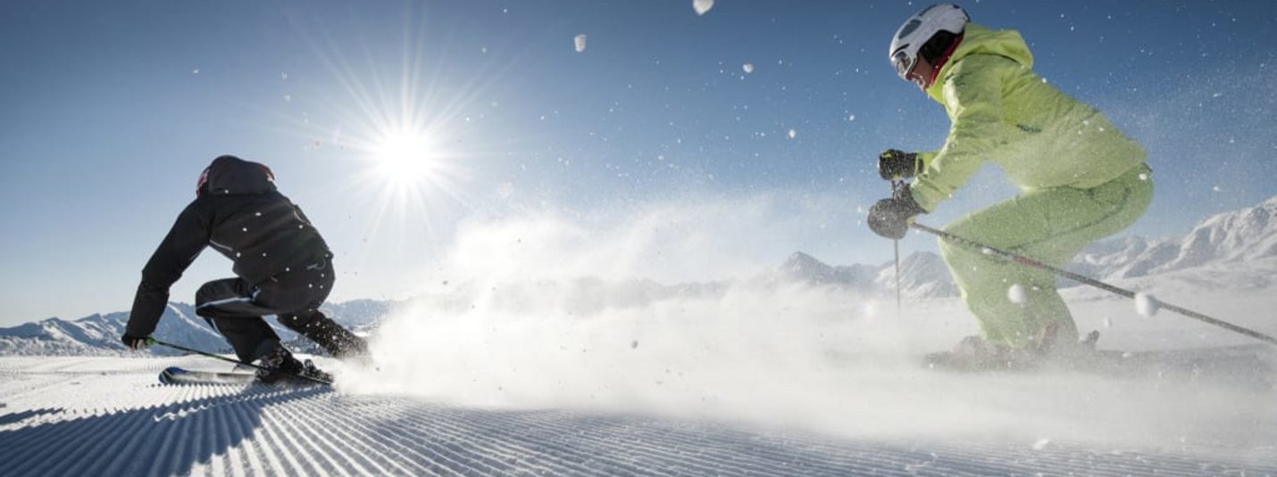 Two skiers skiing down a freshly groomed slope in sunny weather