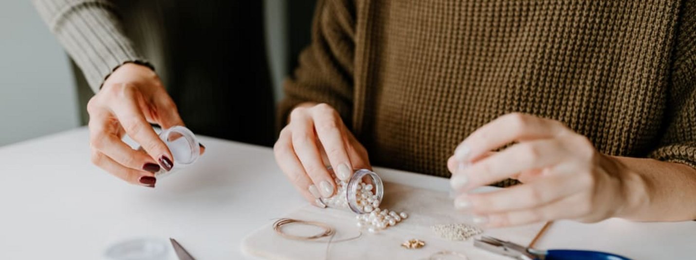 Personen, die Perlen und Schmuckwerkzeuge auf einem Tisch arrangieren