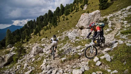 Twee mountainbikers op een rotsachtig bergpad met groene bomen