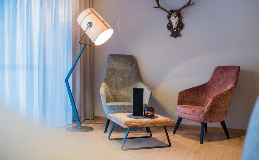 Woonkamer met twee fauteuils, vloerlamp, houten tafel en hertengewei aan de muur