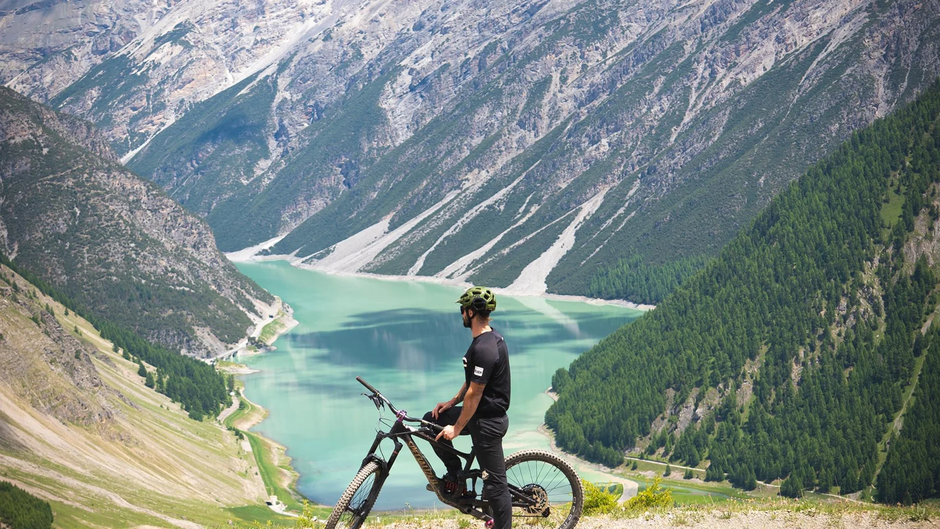 Mann mit Fahrrad blickt auf See und Berge bei sonnigem Wetter