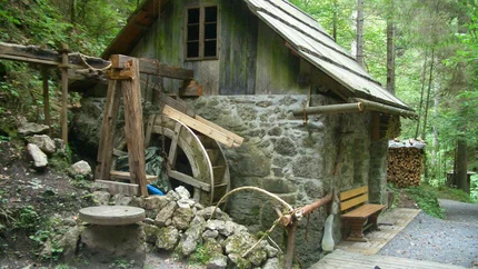 Altes Wassermühlenhaus aus Stein und Holz im Wald mit Bank und Fahrrad