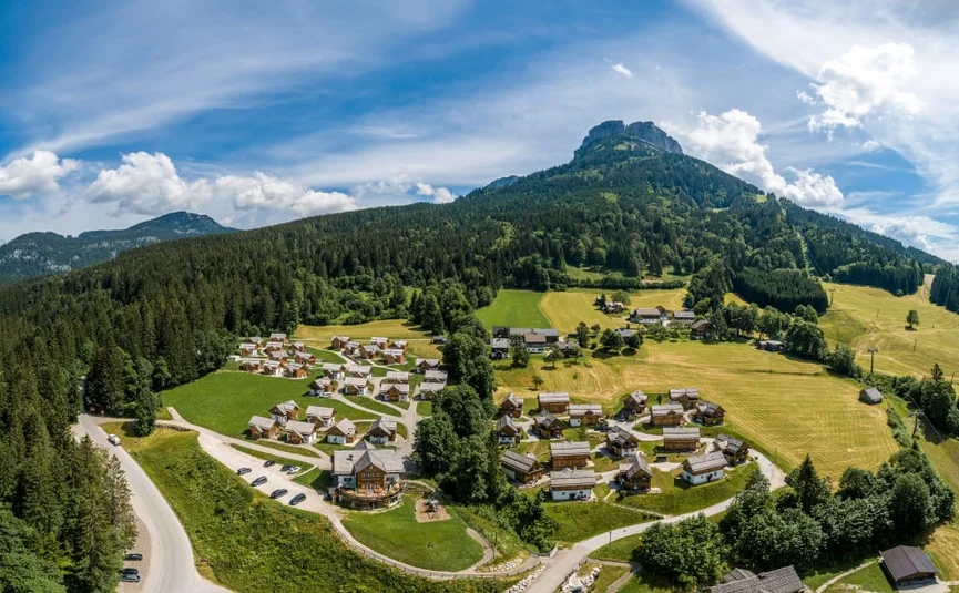 Luftaufnahme eines Bergdorfes mit Häusern, Wiesen und Wäldern unter blauem Himmel
