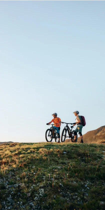 Twee mountainbikers met fietsen op een heuvel onder een heldere lucht