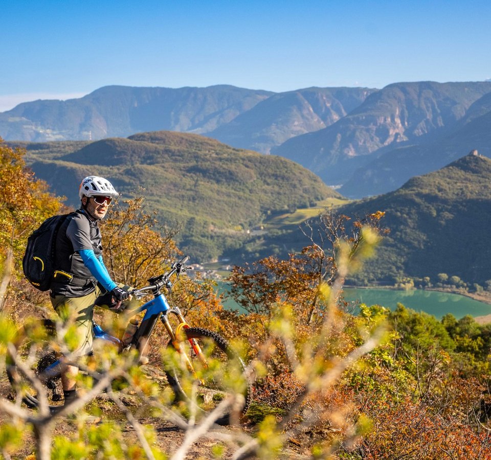 Bike-Spätsommer in Tramin © Antie Braito Mountainbiker mit Helm auf einem Hügel mit Berg- und Seeblick
