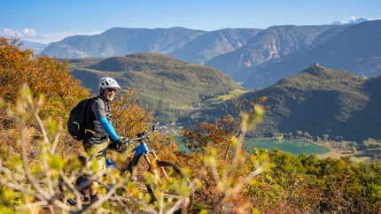 Mountainbiker mit Helm auf einem Hügel mit Berg- und Seeblick
