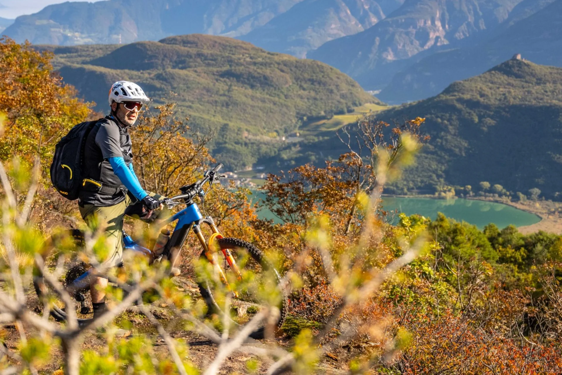 Mountainbiker mit Helm auf einem Hügel mit Berg- und Seeblick