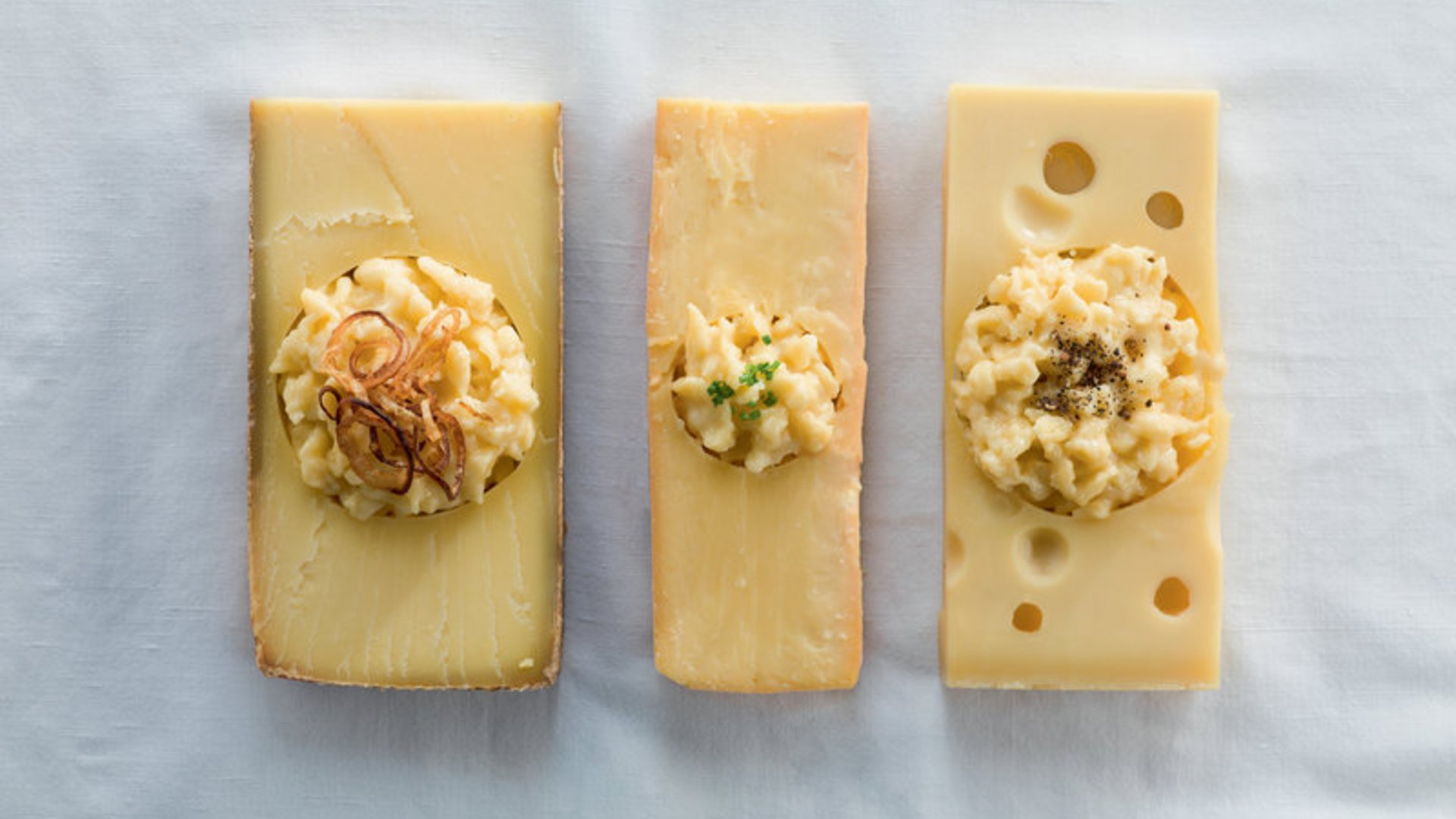 Drei Käsesorten mit Portionen Käsespätzle und Garnitur
