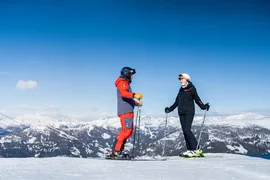 Two skiers against a snowy mountain landscape under a blue sky