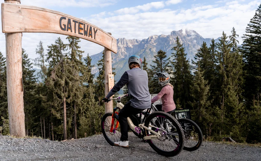 Zwei Mountainbiker mit Helmen an einem Holztor mit Bergblick