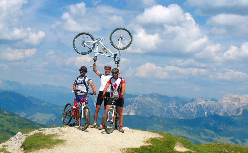 Drei Mountainbiker auf einem Berg mit einem Fahrrad über dem Kopf