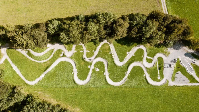 Luftaufnahme eines verschlungenen Fahrradwegs durch eine grüne Wiese