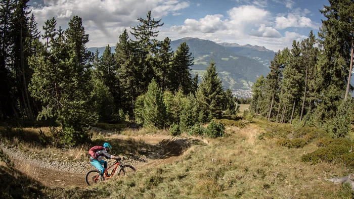 Mountain biker rides on a forest trail in the mountains under cloudy sky