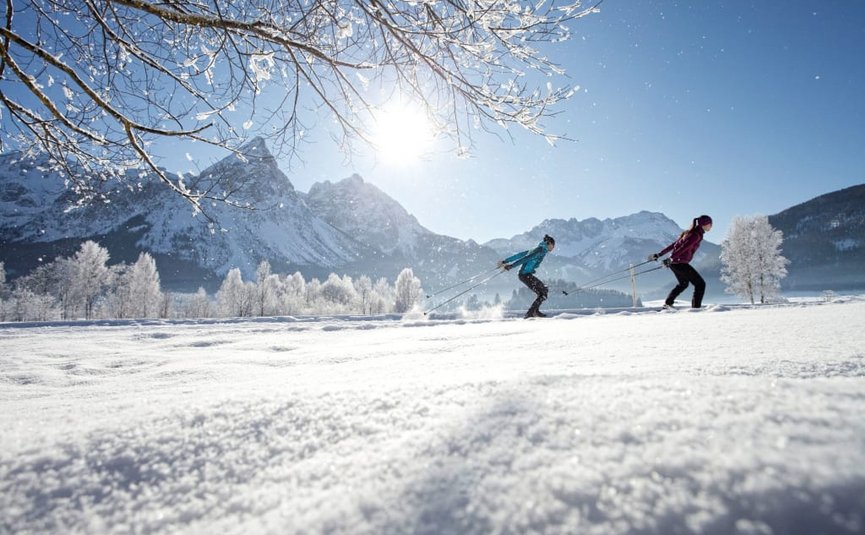 Twee mensen langlaufen in besneeuwde bergvallei onder heldere zon