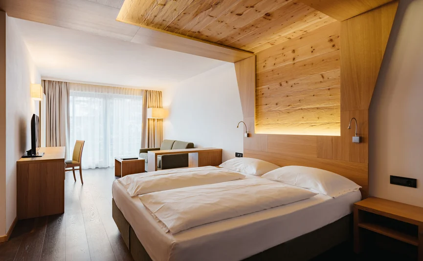 Modernes Hotelzimmer mit Doppelbett, Sofa, Holzverkleidung und großem Fenster