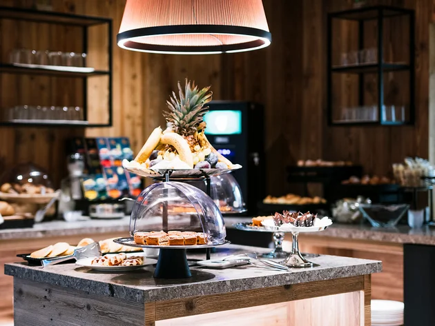 Buffet mit Obst und Gebäck auf einem Holztisch unter einer großen Lampe