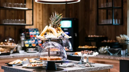 Buffet mit Obst und Gebäck auf einem Holztisch unter einer großen Lampe