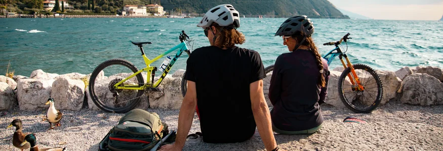 Mountainbiken im Herbst: 5 Top-Regionen für die Saisonverlängerung © David Karg Zwei Fahrradfahrer mit Helmen sitzen am See mit Blick auf Berge und Wasser