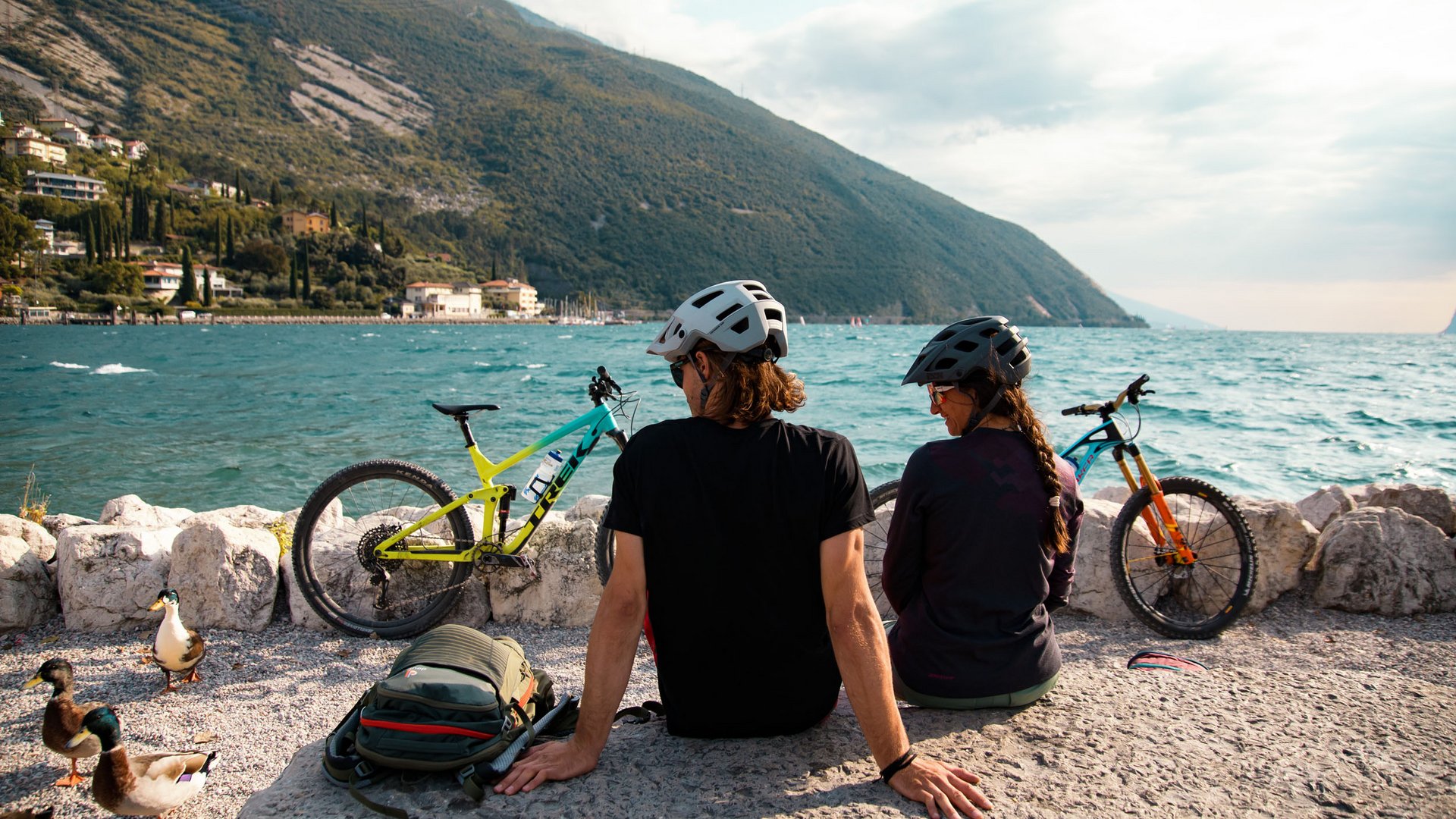 Mountainbike Urlaub für Anfänger
© David Karg Zwei Fahrradfahrer mit Helmen sitzen am See mit Blick auf Berge und Wasser
