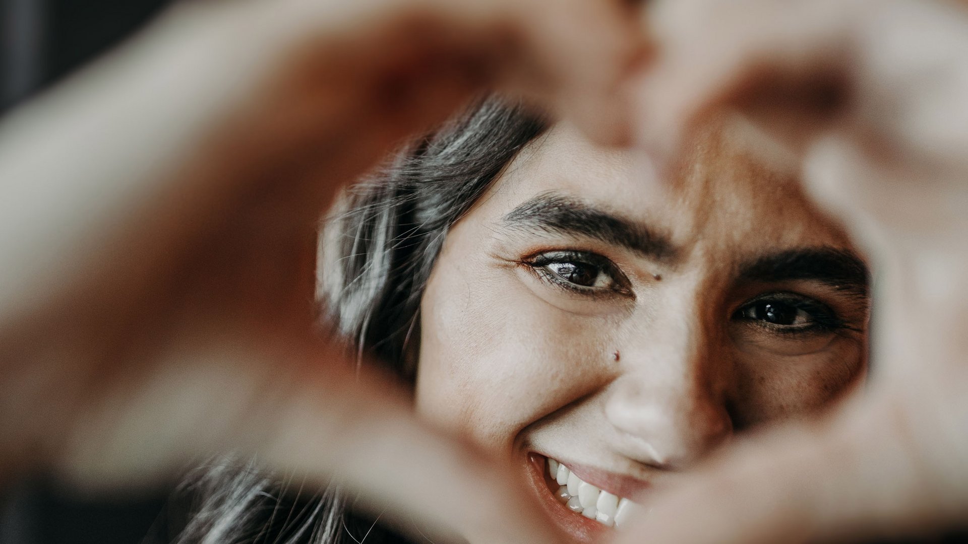 Frau macht mit Händen ein Herz und lächelt in die Kamera