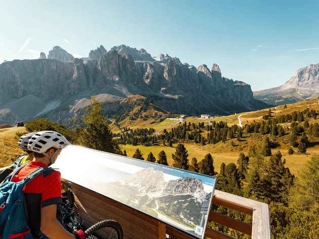 Radfahrer liest Informationstafel mit Blick auf Berglandschaft