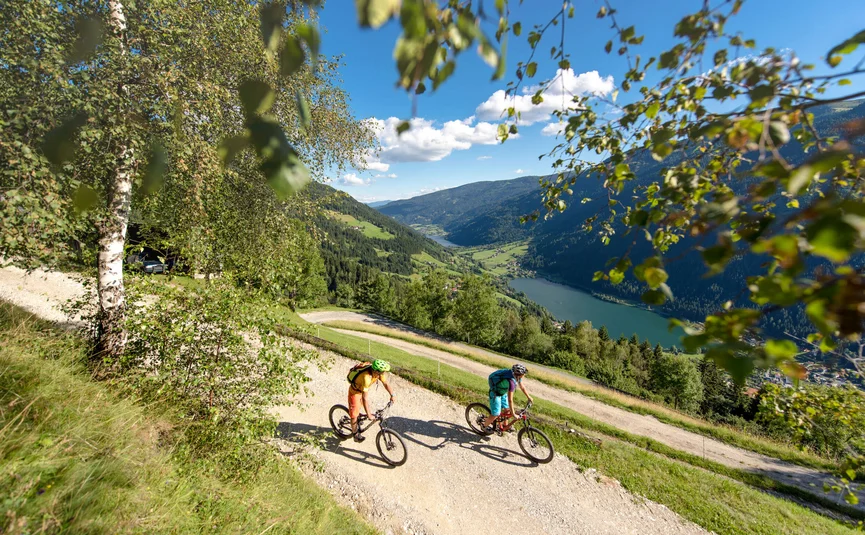 Zwei Mountainbiker fahren auf Bergweg mit Blick auf Tal und See