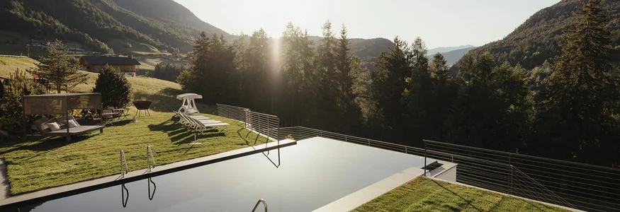 Infinity zwembad met ligstoelen en berglandschap bij zonsondergang