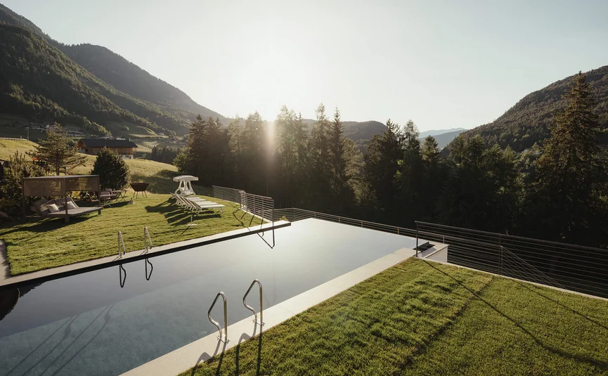 Infinity zwembad met ligstoelen en berglandschap bij zonsondergang