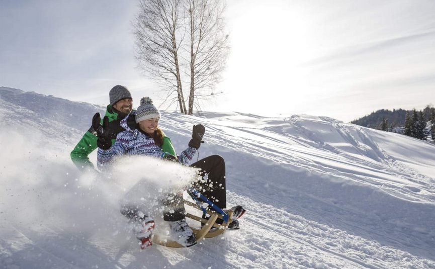 Twee mensen sleeën van een besneeuwde heuvel op een zonnige dag