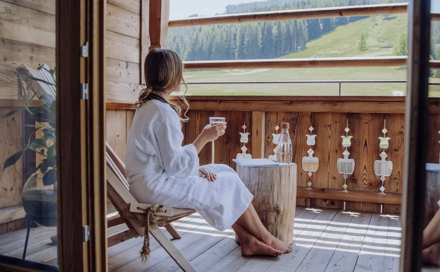Frau im Bademantel entspannt auf Balkon mit Bergblick
