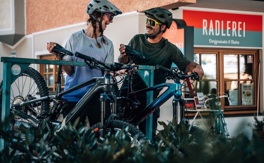 Bike Boutique Hotel Lindenhof **** © Jens Scheibe Zwei Radfahrer mit Helmen lachen vor einer Fahrradwerkstatt