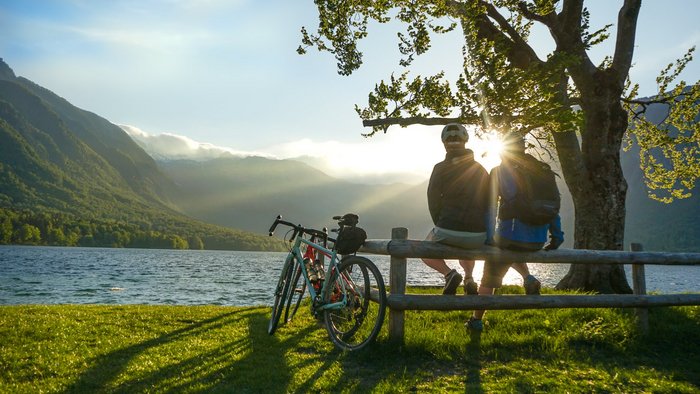 Zwei Radfahrer sitzen am Seeufer bei Sonnenuntergang mit Blick auf Berge
