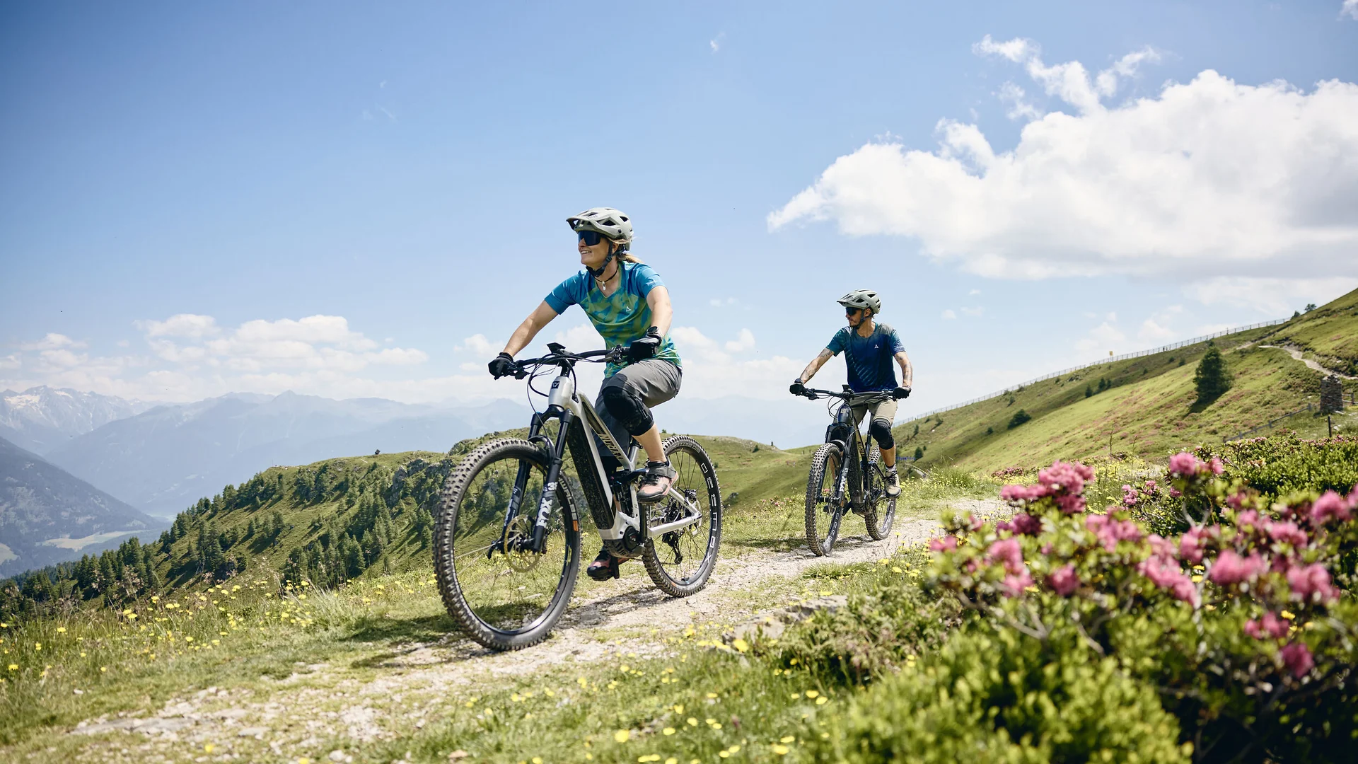 Zwei Personen fahren auf Bergpfad mit E-Mountainbikes bei sonnigem Wetter