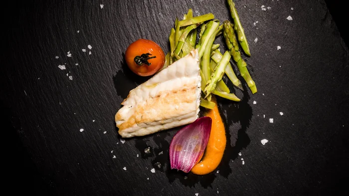 Gegrilde visfilet met asperges, tomaat en saus op zwarte steen