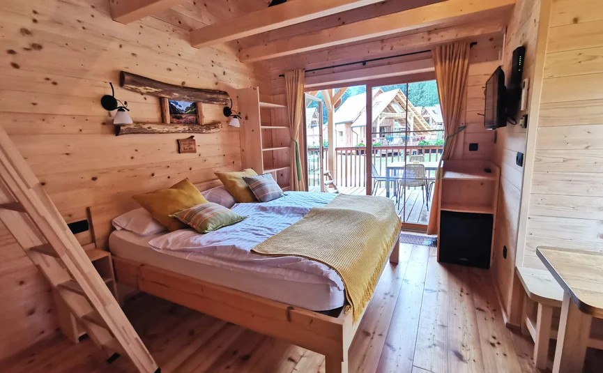 Gemütliches Holzschlafzimmer mit Doppelbett und Balkon mit Blick auf andere Hütten