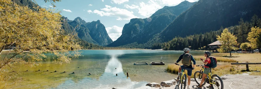 Spätsommer- & Herbstbiken in Toblach © David Karg Zwei Radfahrer an einem See mit Bergen bei sonnigem Wetter