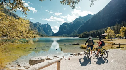 Zwei Radfahrer an einem See mit Bergen bei sonnigem Wetter